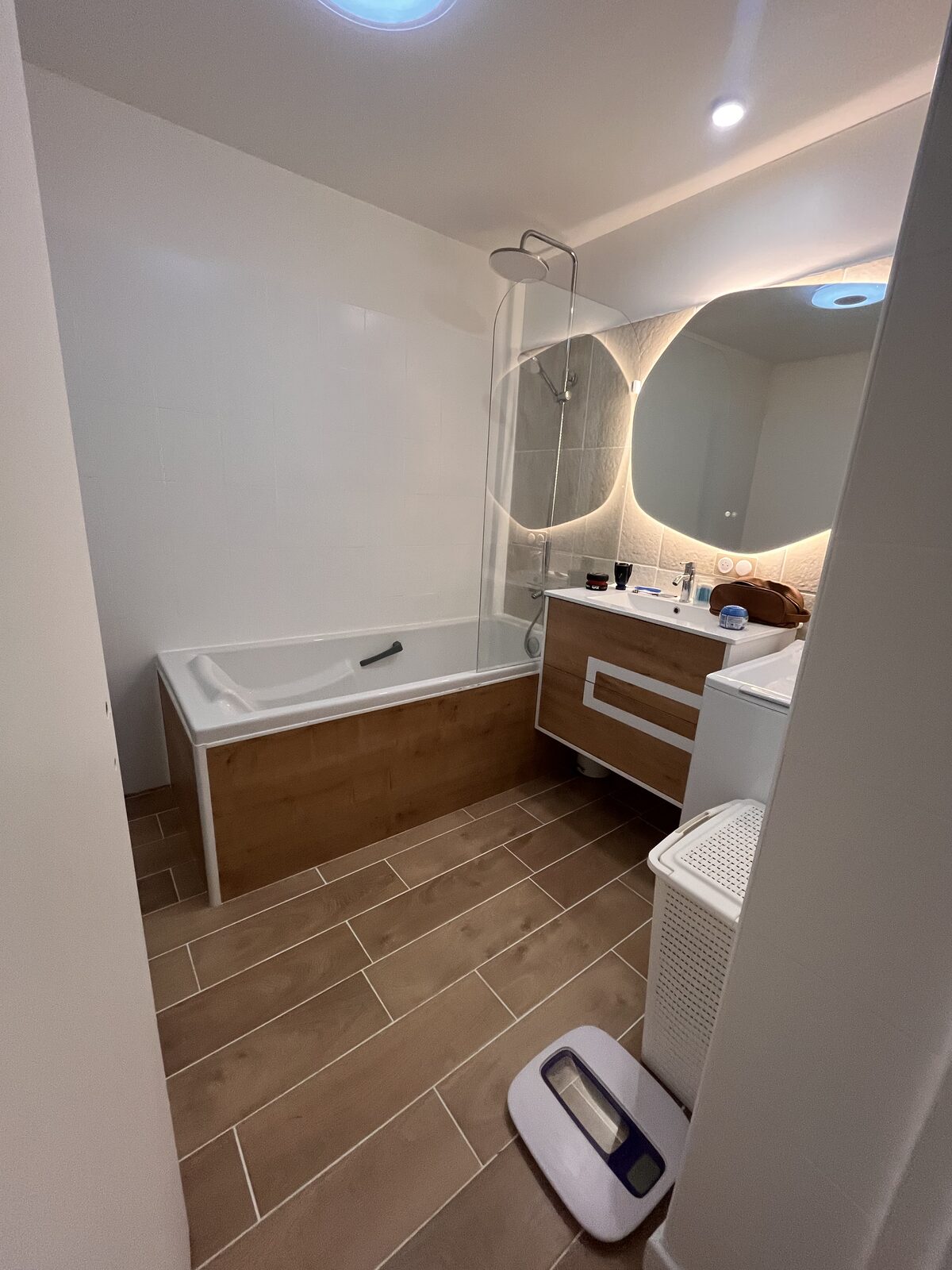 Salle de bain rénovée avec baignoire, pare-douche, meuble vasque bois et carrelage effet bois
